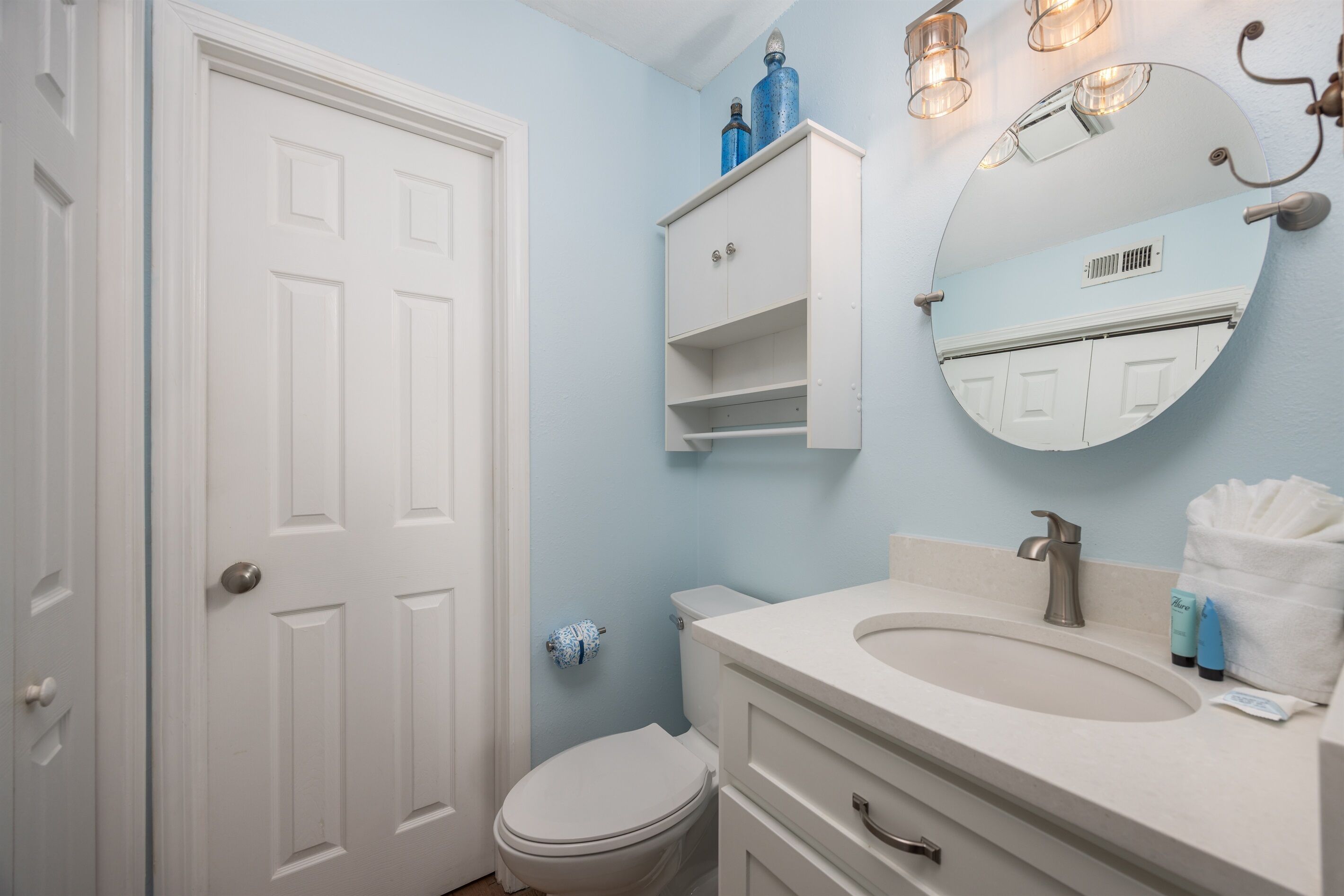 Een badkamer met een wit toilet, een wastafel met een spiegel erboven en een kastje met blauwe flessen.