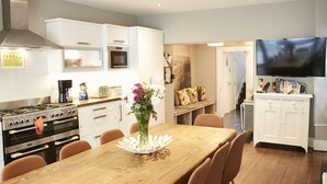 Una cocina moderna con armarios blancos, una mesa de comedor de madera y un televisor de pantalla plana montado sobre ella.