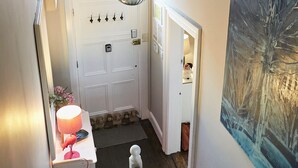 Un pasillo con una puerta blanca, un cuadro en la pared, una lámpara colgante y una mesita con lámpara.