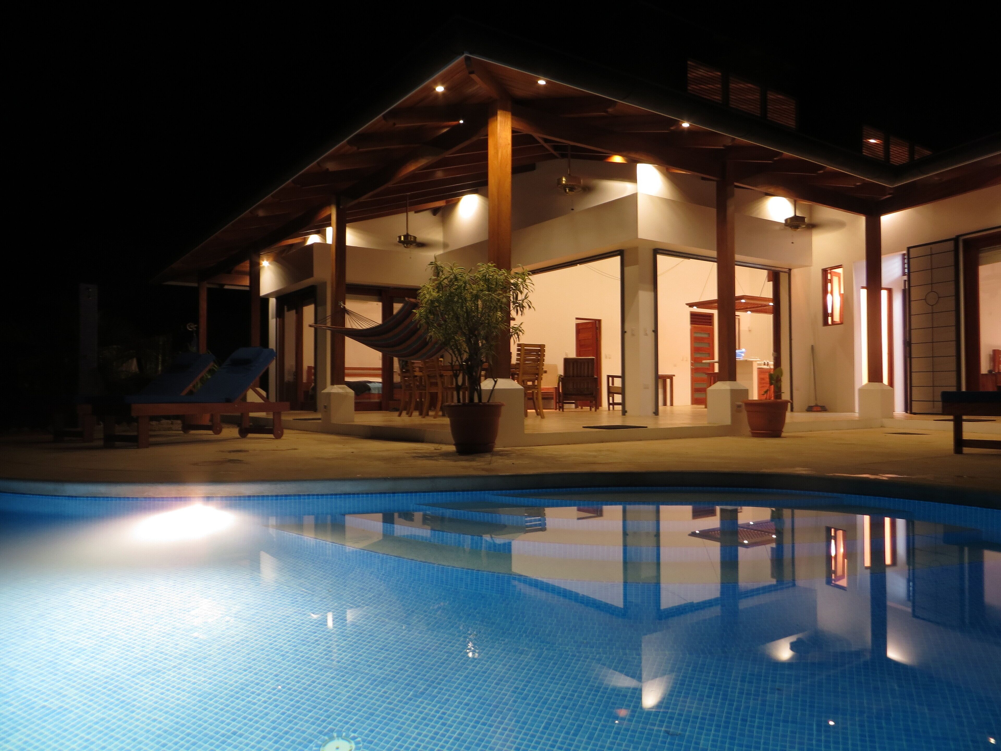 Ein Poolbereich mit klarem Pool, Holzdeck und einem Gebäude mit großen Fenstern und Türen.