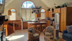 A spacious kitchen with wooden cabinets, a large island, and a dining area with wicker chairs. - BLUE HAVEN-COROLLA-OBX (Corolla)