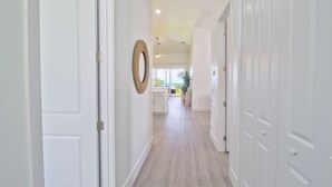 Un pasillo con puertas blancas, suelo de madera y vista a un área de cocina en la distancia.