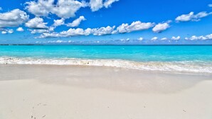 Una playa con agua turquesa cristalina y una orilla arenosa bajo un cielo azul brillante con nubes dispersas.