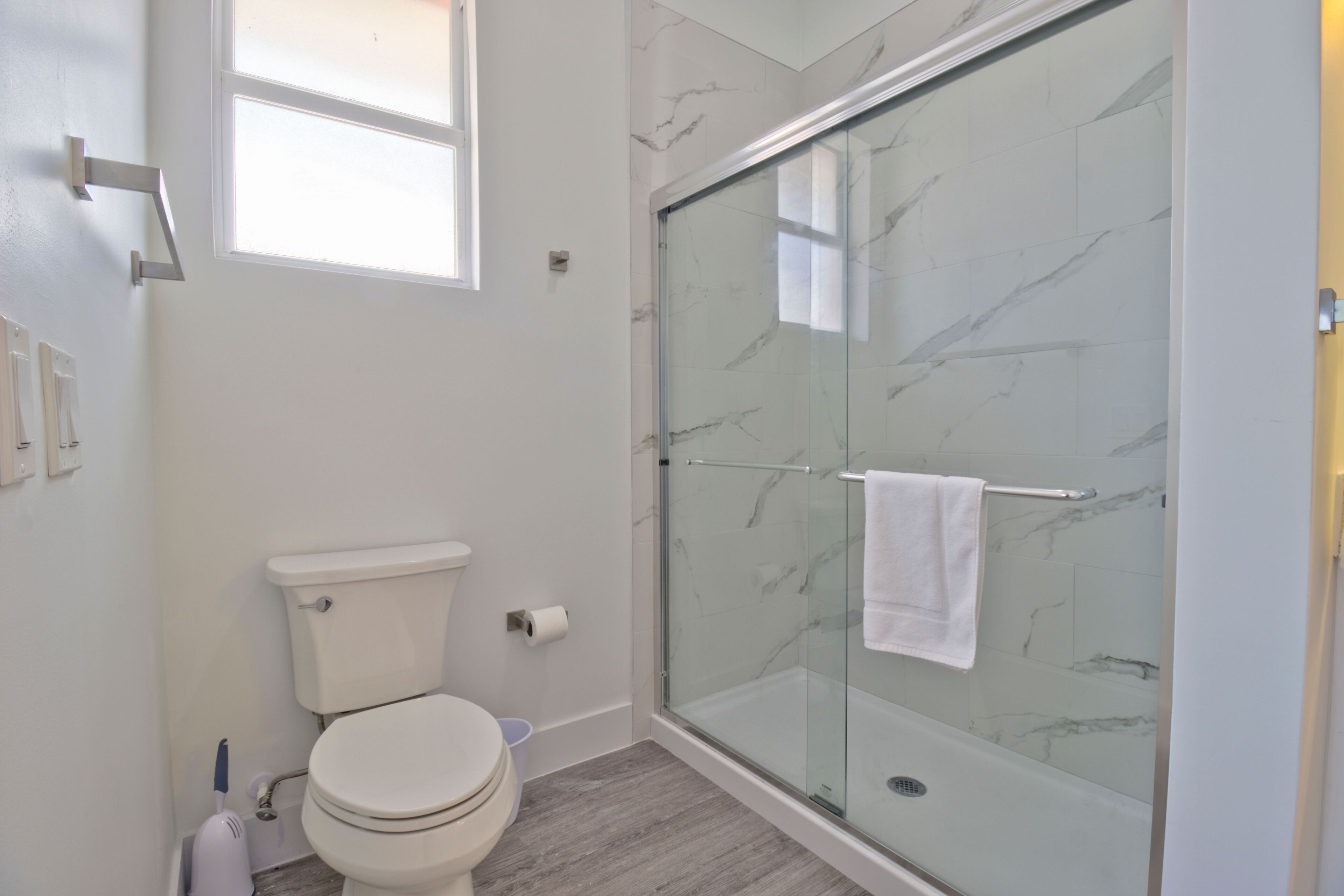 Un baño con inodoro, cabina de ducha de vidrio y pared con azulejos de mármol.