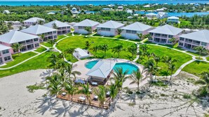 Un resort con varias edificaciones, una piscina central y una zona de playa con palmeras.