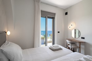 A hotel room with a bed, a desk with a chair, a mirror, and a view of the sea.
