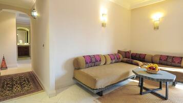 A living room with a sofa, a small table with a fruit bowl, and two wall-mounted lights.