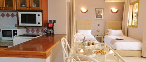 A hotel room with a kitchenette, a dining area with a table and chairs, a bed, and a bathroom.