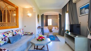 Una habitación de hotel moderna con sofá, una mesita con un florero, televisor y cama con mesita de noche.