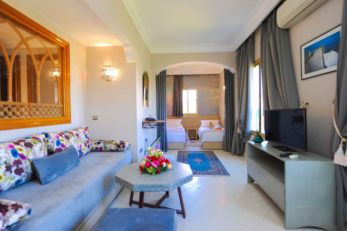 A modern hotel room with a sofa, a small table with a vase of flowers, a TV, and a bed with a nightstand.