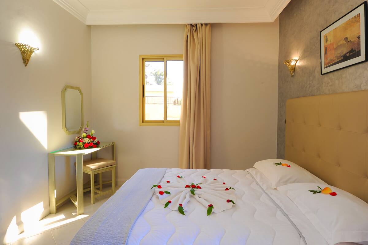 A hotel room with a bed, a desk, a chair, a window with curtains, and a wall-mounted picture.