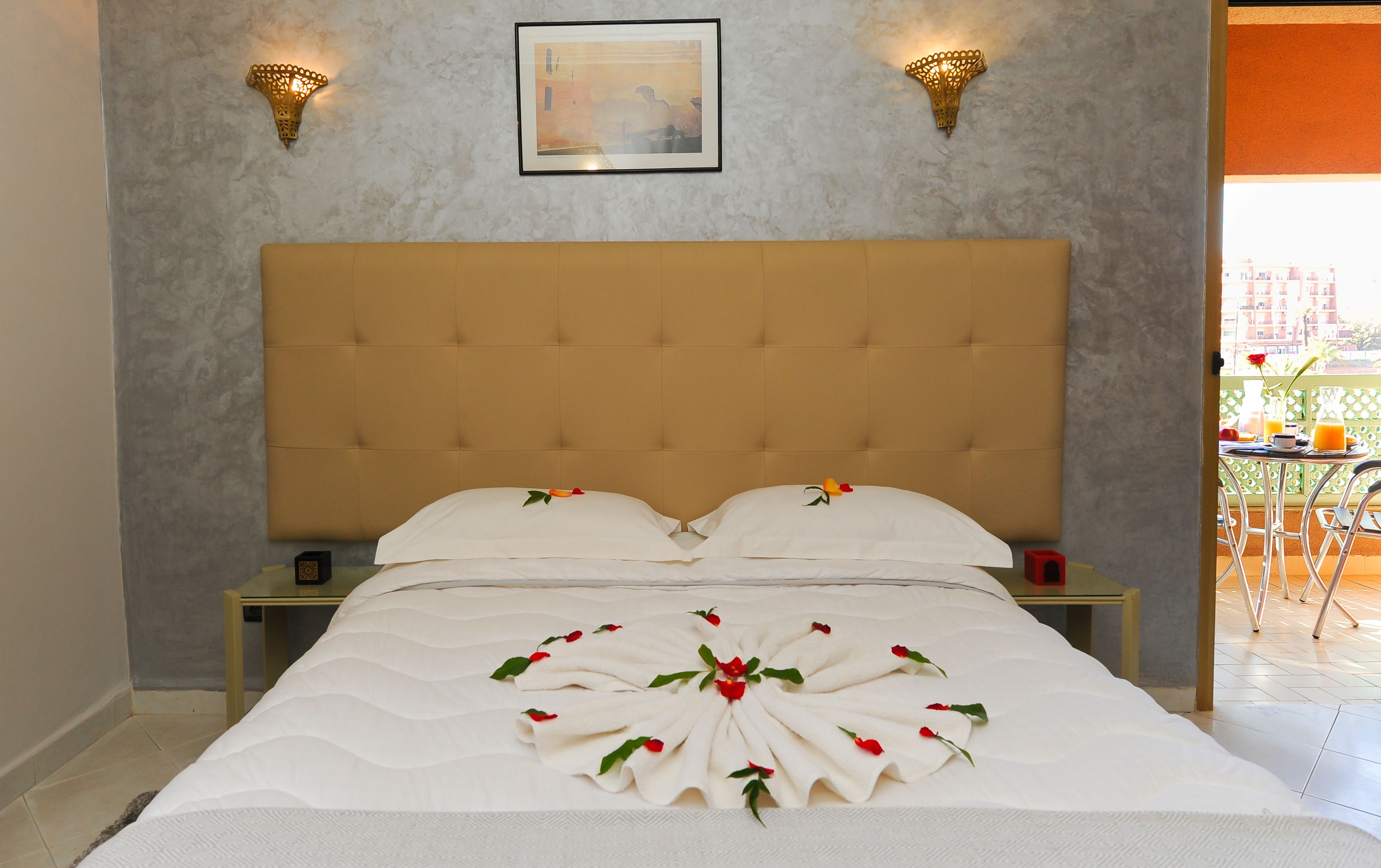 A neatly made bed with a decorative towel arrangement, two wall-mounted lights, and a framed picture on the wall.