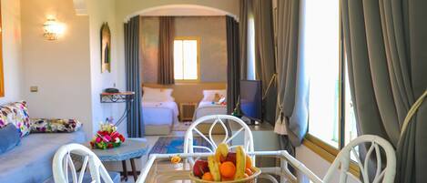 A hotel room with a dining table, a sofa, a bed, and a window with curtains.