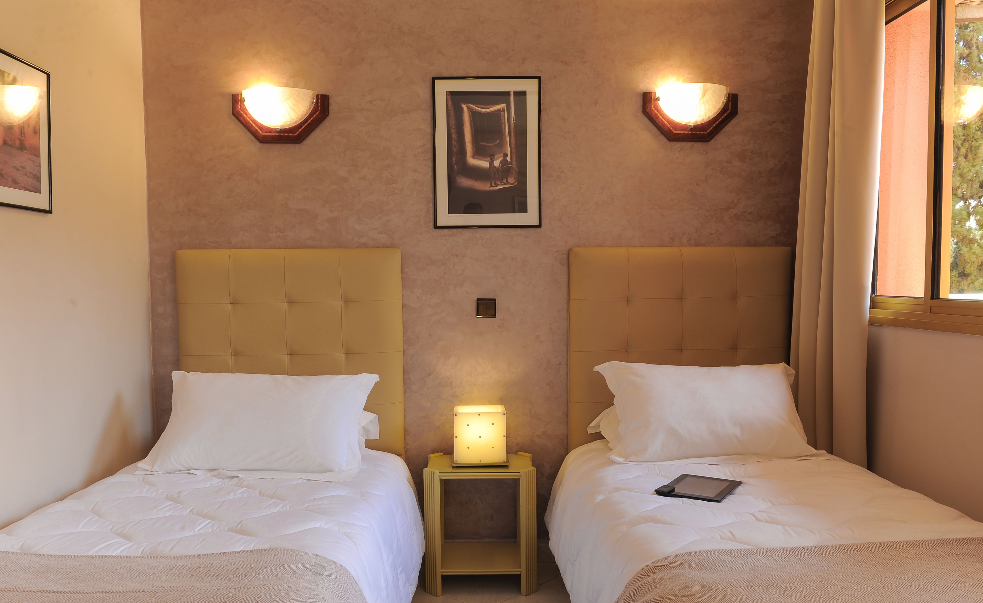 Habitació d'hotel amb dos llits, una tauleta de nit amb una làmpada, i un quadre al mur.