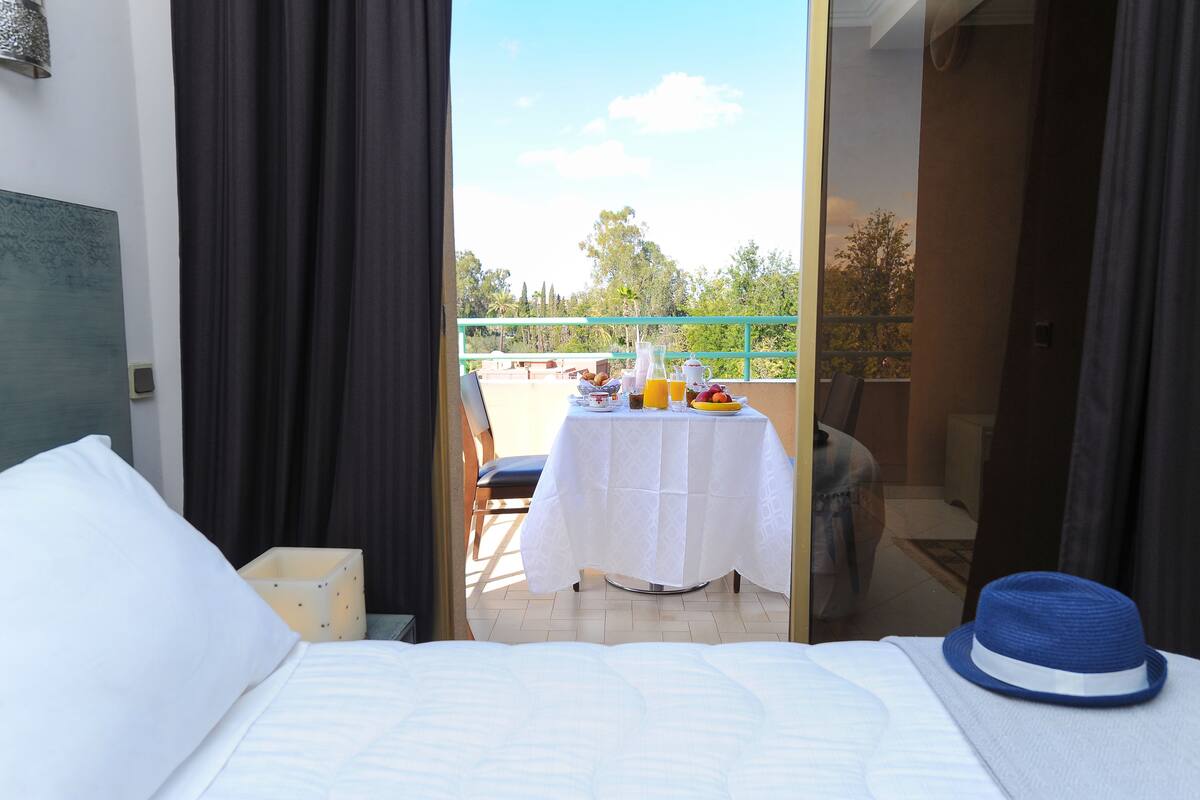 A hotel room with a bed, a table with breakfast items, and a view of the outdoors.