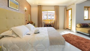 Una habitación de hotel con una cama grande, una mesita, un sofá y un ventanal con cortinas.