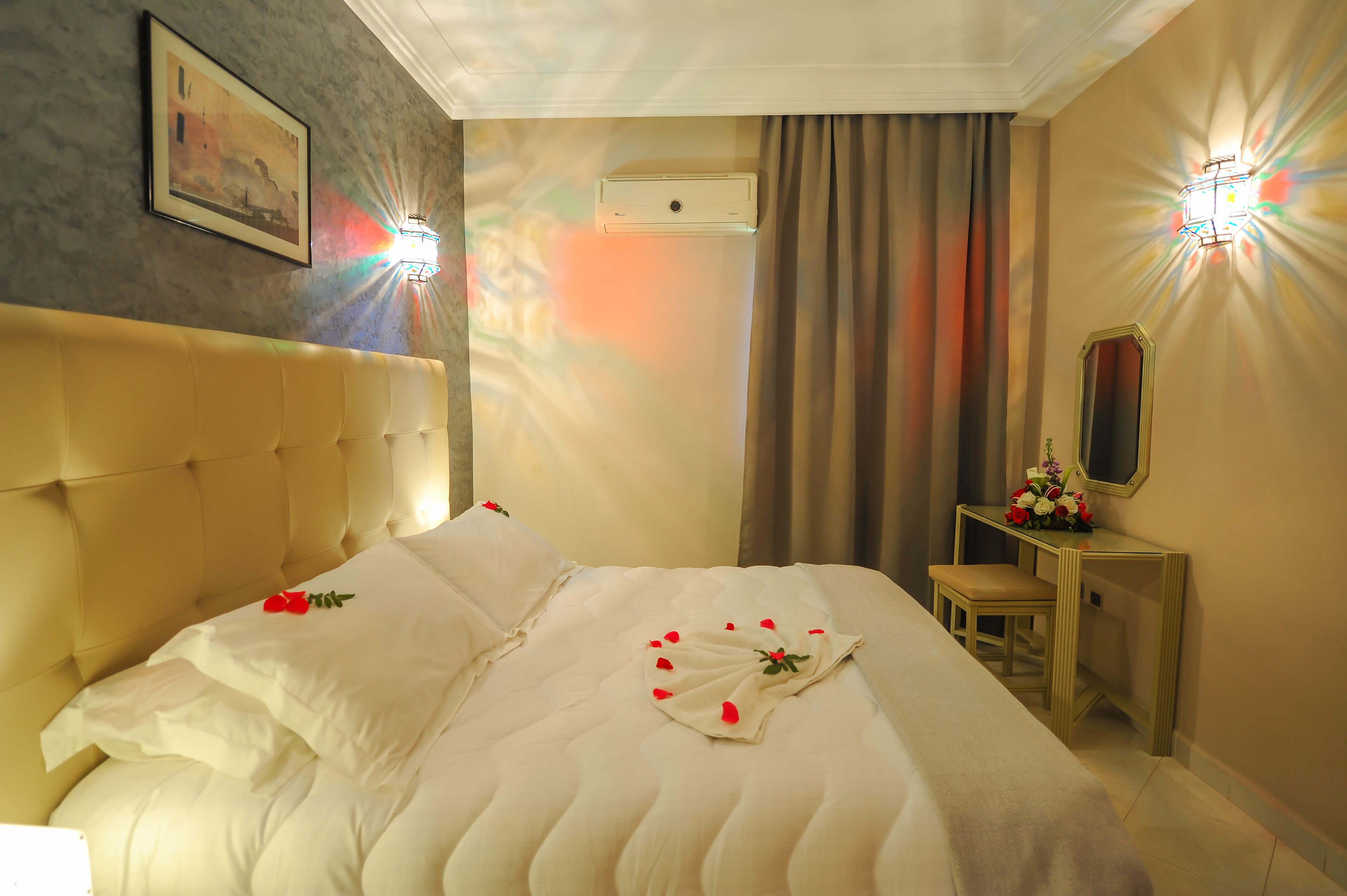 A hotel room with a large bed, a bedside table with a mirror, and a wall-mounted air conditioner.