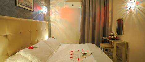 A hotel room with a large bed, a bedside table with a mirror, and a wall-mounted air conditioner.