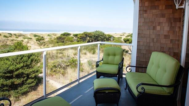 Ein Balkon mit Korbstühlen und passendem Hocker, mit Blick auf eine Küstenlandschaft mit Dünen und Vegetation.