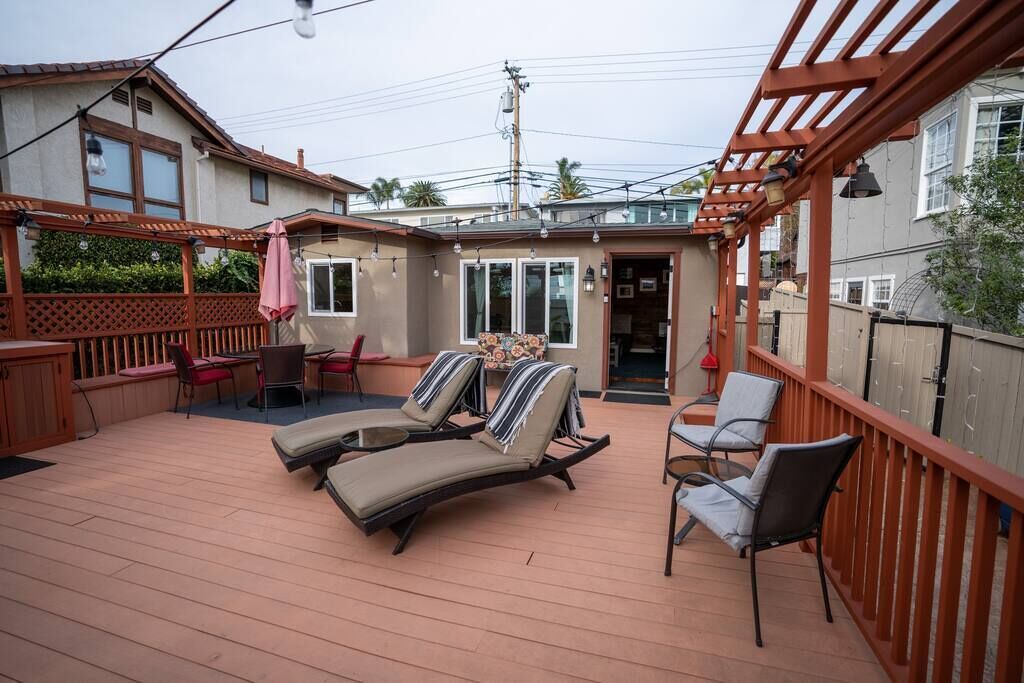 A covered outdoor deck with lounge chairs and a table, surrounded by a wooden deck and a pergola.