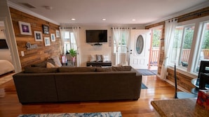 A living room with a large sectional sofa, a flat-screen TV mounted on the wall, and a wooden accent wall. - Walk everywhere; Beach 300 steps (Laguna Beach)