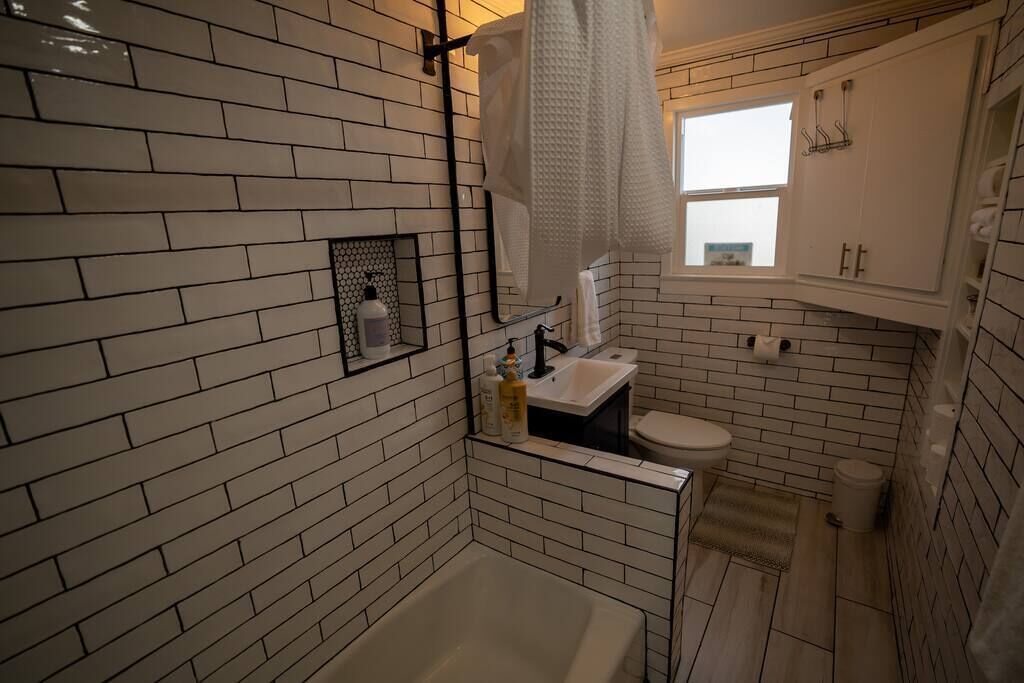 A compact bathroom with a white brick wall, a bathtub, a toilet, and a window.