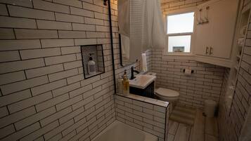 A compact bathroom with a white brick wall, a bathtub, a toilet, and a window.