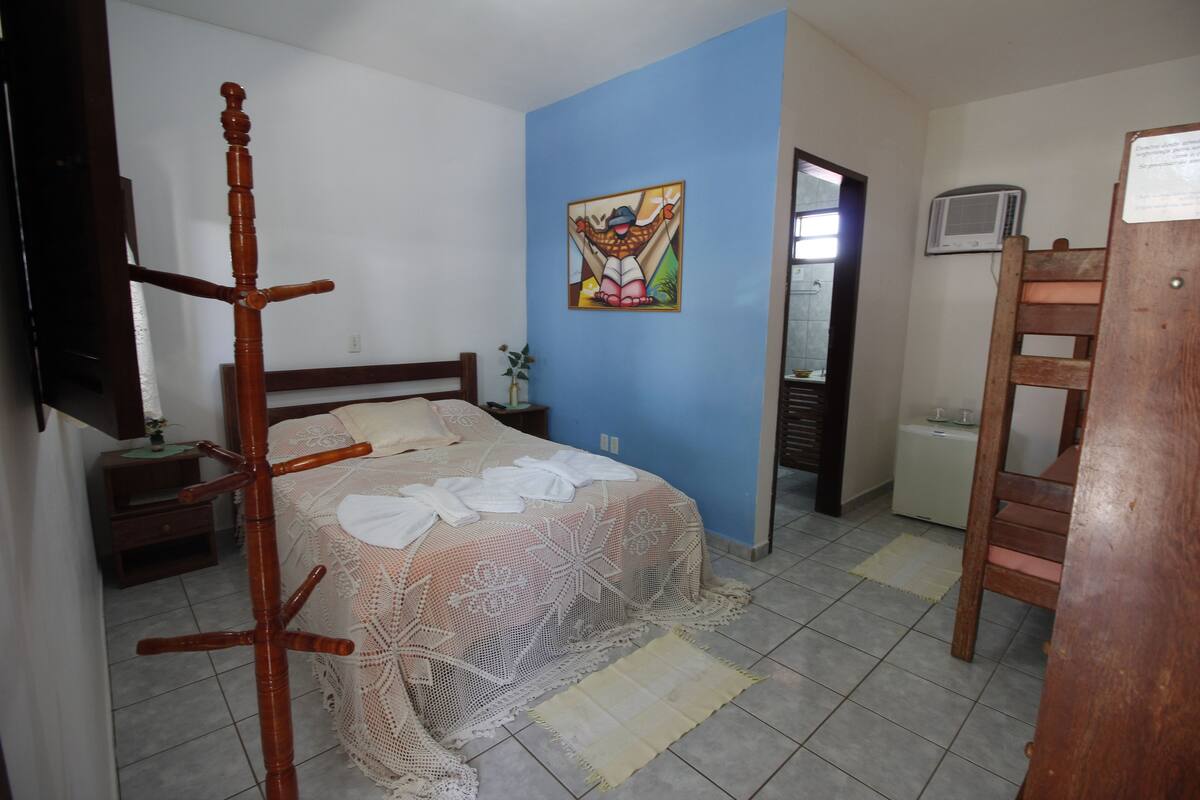 Un dormitorio con cama, una silla de madera, una mesita de noche, una pequeña mesa y un televisor instalado en la pared.