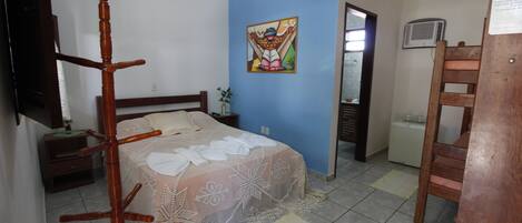 A bedroom with a bed, a wooden chair, a nightstand, a small table, and a wall-mounted TV.