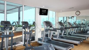 A gym with multiple treadmills, a TV screen displaying "FOUR POINTS BY SHERATON," and large windows offering a view of the outdoors. - Four Points by Sheraton Veracruz (Boca del Río)