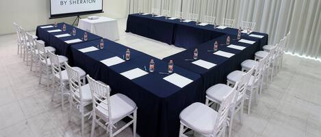 A conference room with a long table, white chairs, and a screen displaying "FOUR POINTS BY SHERATON".