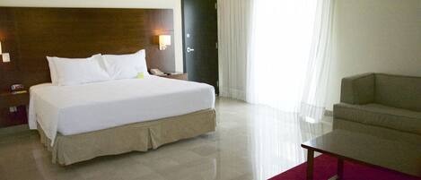 A hotel room with a large bed, a desk, a chair, and a door.