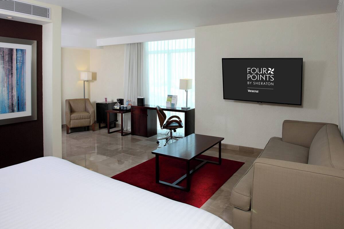 Een hotelkamer met een bed, een bureau, een stoel, een bank en een aan de muur bevestigde televisie.