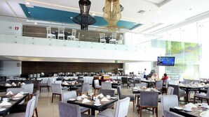 A spacious dining area with multiple tables and chairs, a second-floor balcony with chairs, and a large window with a view. - Four Points by Sheraton Veracruz (Boca del Río)