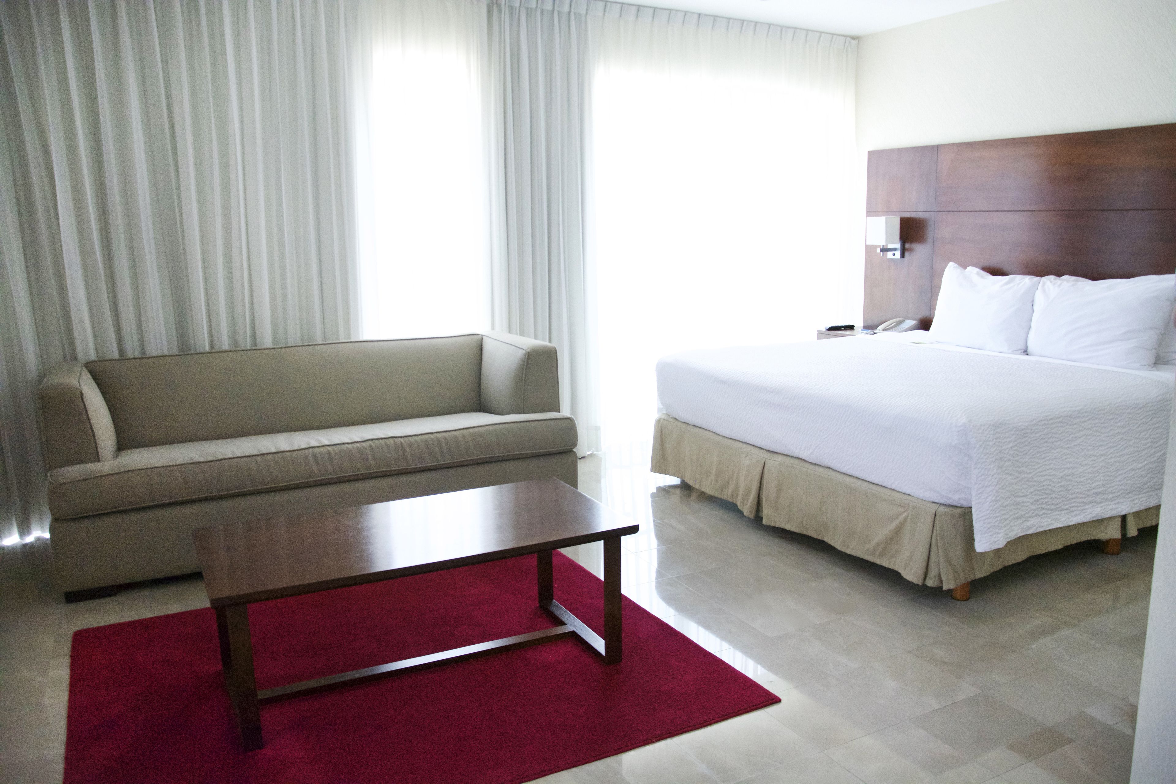 A hotel room with a bed, a sofa, a coffee table, and a red rug.