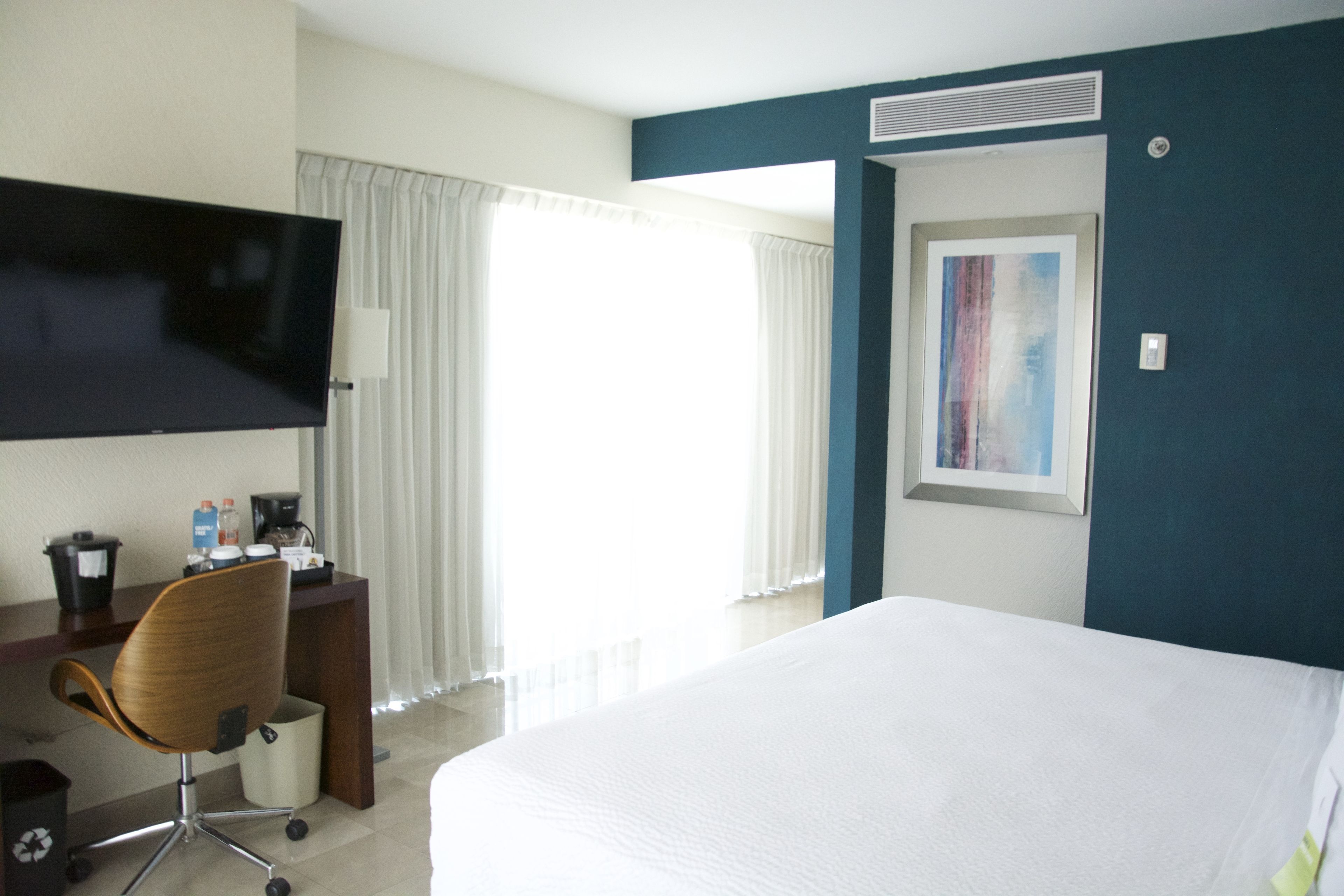 A hotel room with a large bed, a desk with a chair, a flat-screen TV, and a painting on the wall.