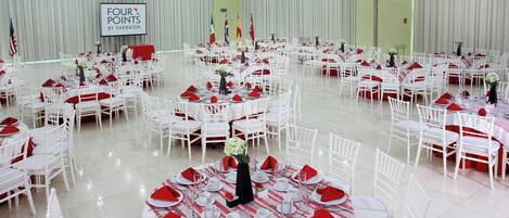 A large banquet hall with multiple round tables set for a formal event, featuring white chairs and red napkins.