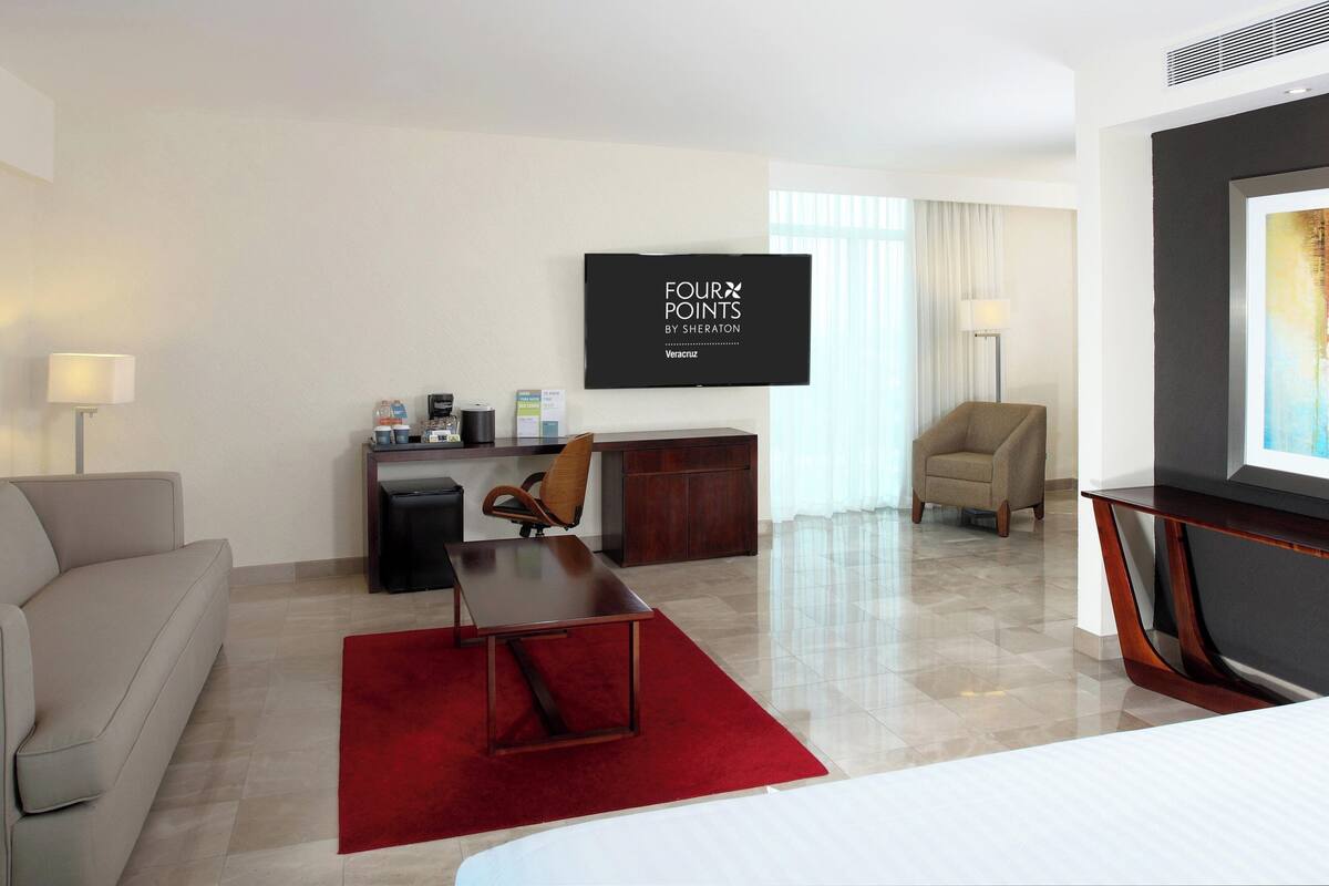 Een hotelkamer met een televisie, een bank, een bureau, een stoel en een rood tapijt.