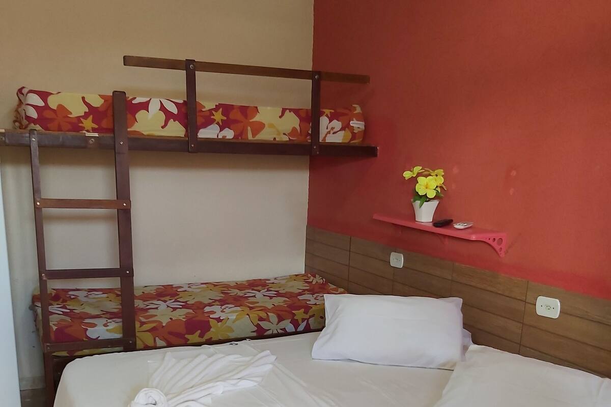 Une chambre d’hôtel avec un lit superposé, une table de chevet ornée d’un vase de fleurs et des lits parfaitement faits.