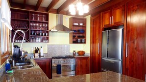 A kitchen with wooden cabinets, a stainless steel refrigerator, a stove, and granite countertops. - Casa Del Mar (Tierra Oscura)