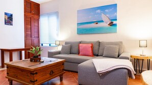 Uma sala de estar com um sofá cinza, uma mesa de centro de madeira e uma pintura de um veleiro na praia.