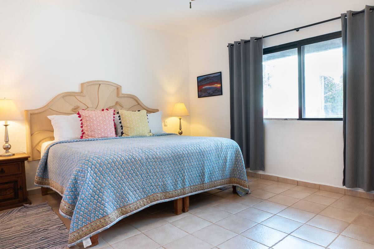 Ein Schlafzimmer mit einem Bett, zwei Nachttischlampen, einem Fenster mit Vorhängen und einem Teppich.