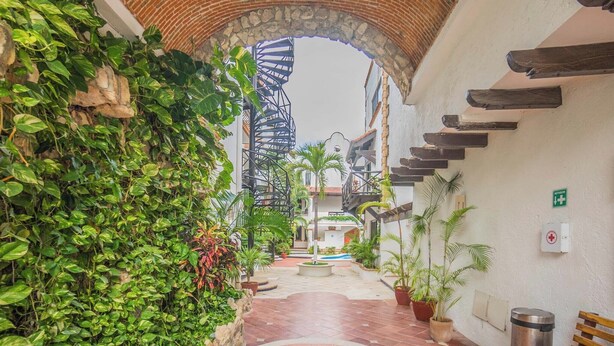 Um pátio com arco de tijolos, vasos de plantas, escada em espiral e piso de azulejos.