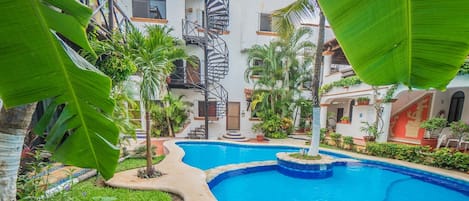 A swimming pool surrounded by lush greenery and a spiral staircase leading to an upper level.
