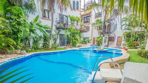 Piscina rodeada por vegetação exuberante e um edifício com várias andares e varandas.