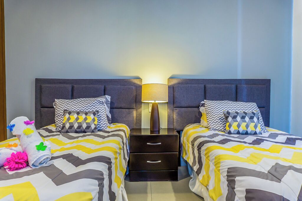 A hotel room with two beds, each with a patterned bedspread, a nightstand with a lamp, and a decorative item on the left bed.