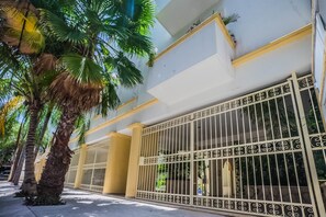 Een gebouw met een witte gevel, decoratieve metalen poorten en palmbomen langs de stoep.