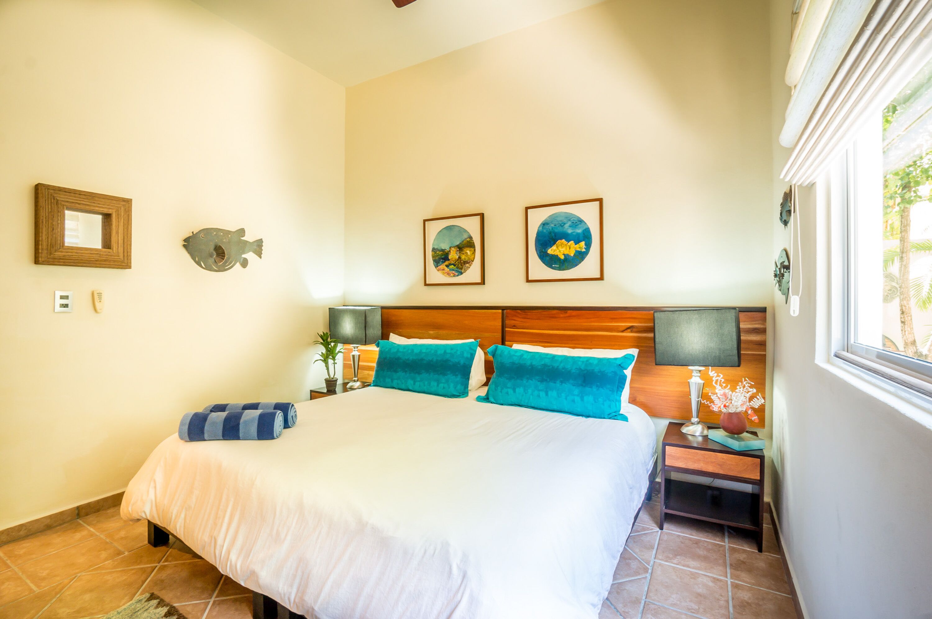 A neatly made bed with white and teal bedding, a wooden headboard, and two wall-mounted fish-themed decorations.