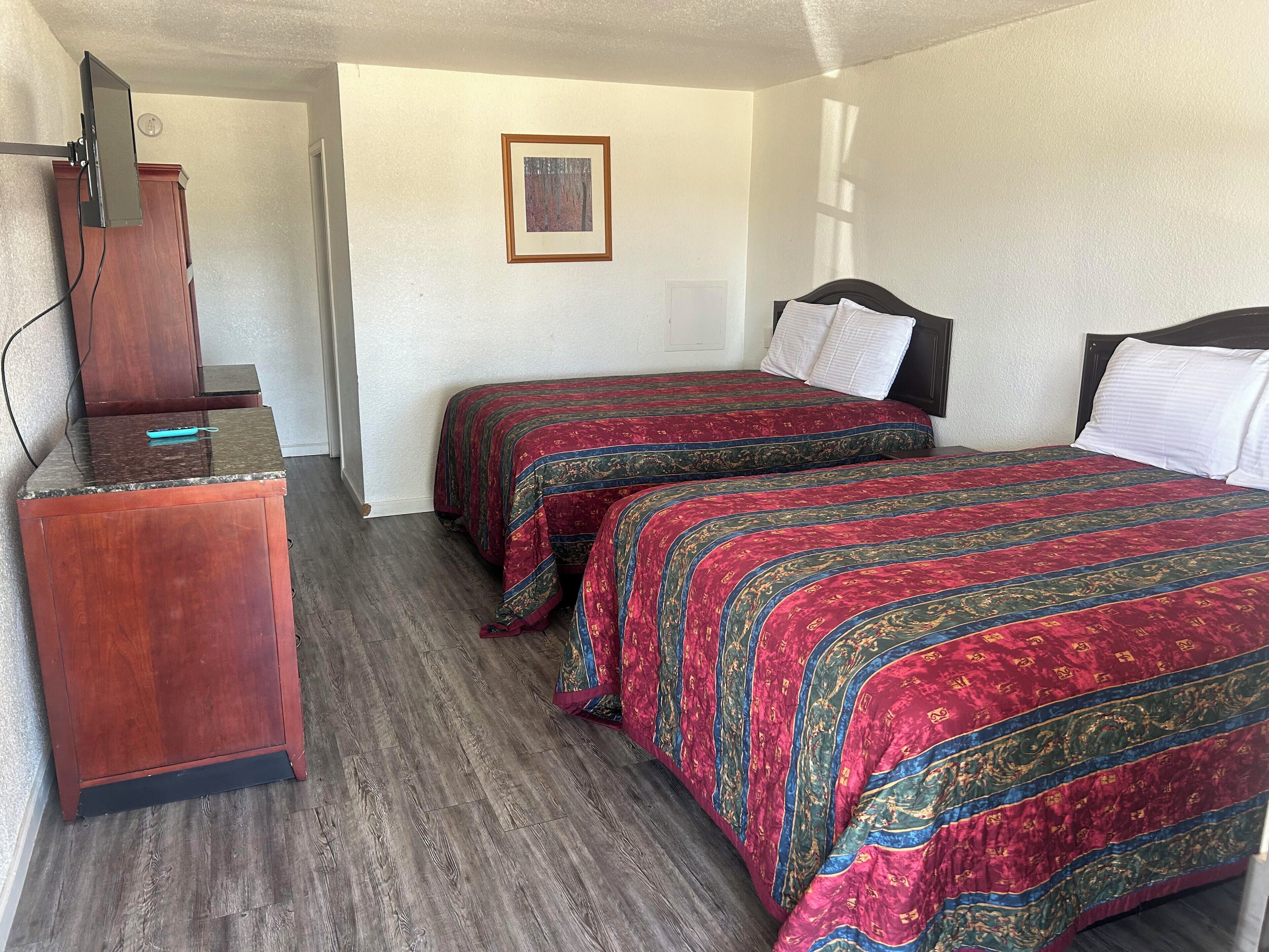 A bedroom with two beds, a wooden dresser, a framed picture on the wall, and a TV mounted on the wall.