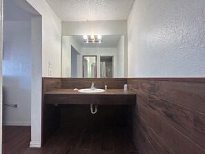 A bathroom with a wooden vanity, a sink, and a mirror with lights above it.